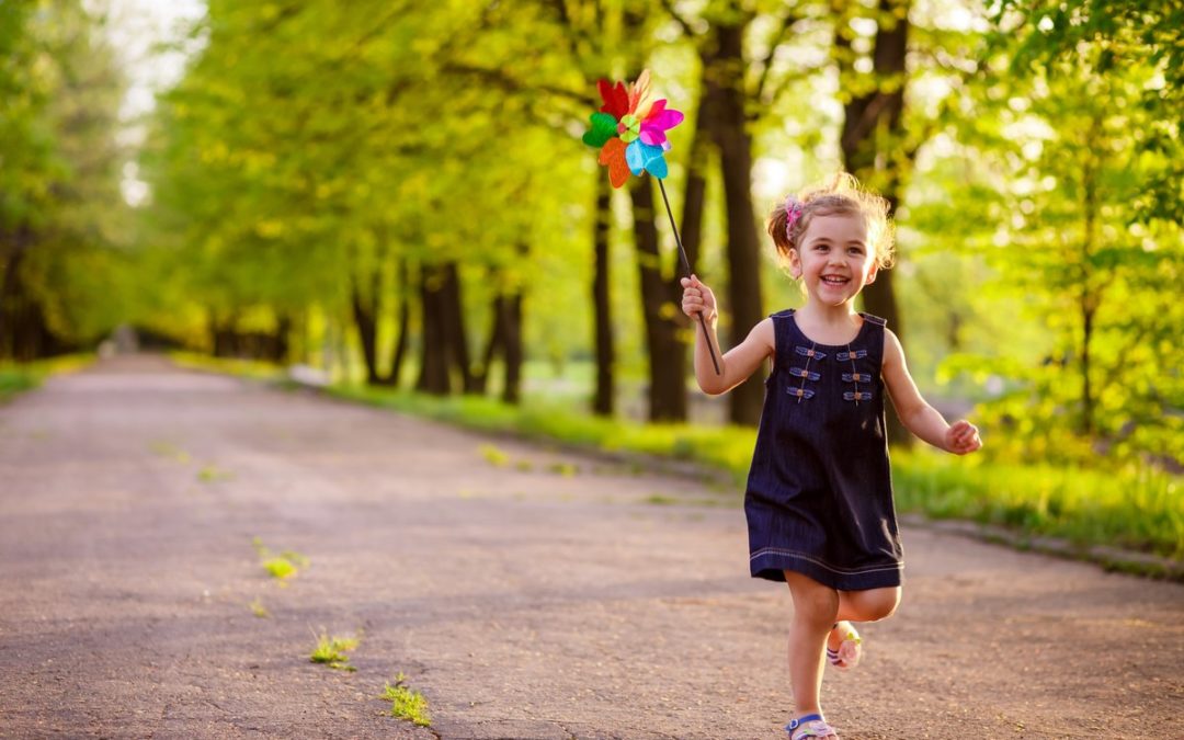 Happy child running on tree-lined path holding colorful pinwheel, representing joy and smiles.